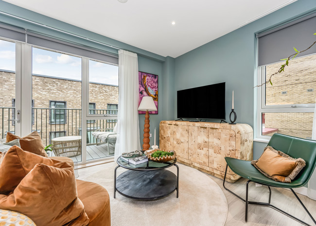A contemporary living room featuring a large TV, sofa and arm chair, and plenty of natural light from the private balcony.