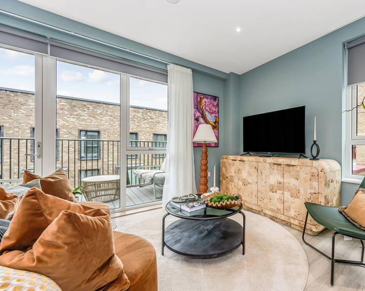 A contemporary living room featuring a large TV, sofa and arm chair, and plenty of natural light from the private balcony.