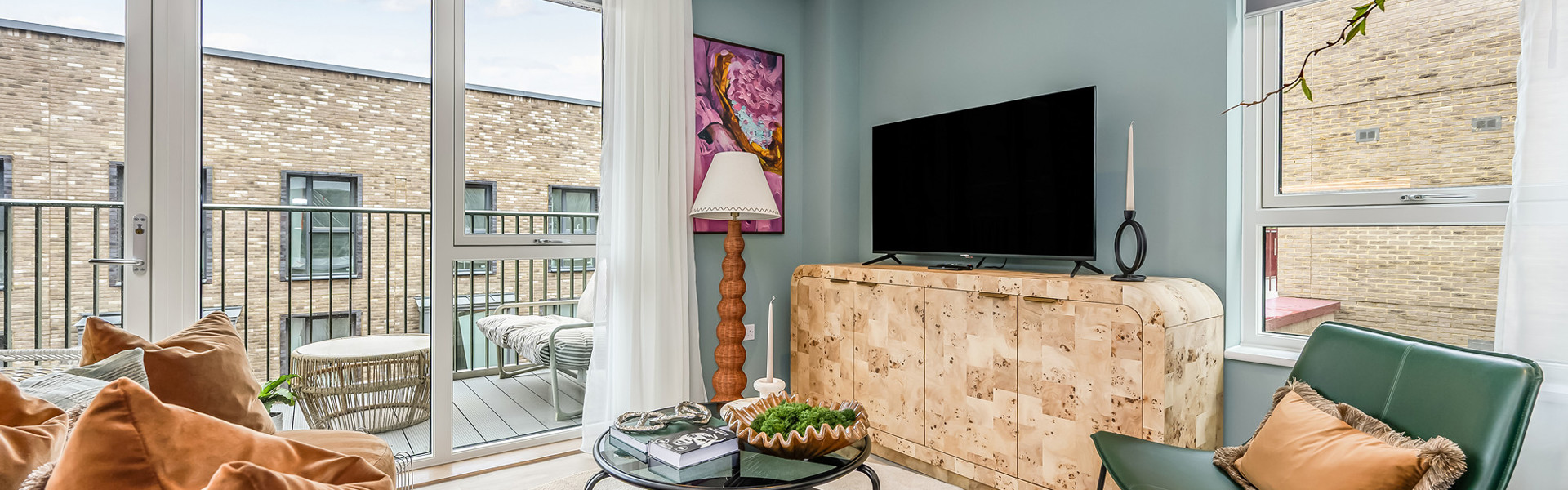 A contemporary living room featuring a large TV, sofa and arm chair, and plenty of natural light from the private balcony.