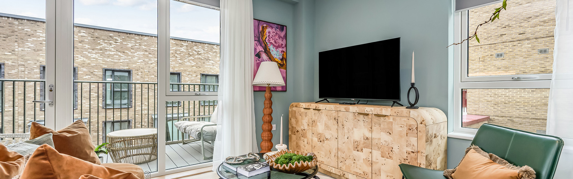 A contemporary living room featuring a large TV, sofa and arm chair, and plenty of natural light from the private balcony.
