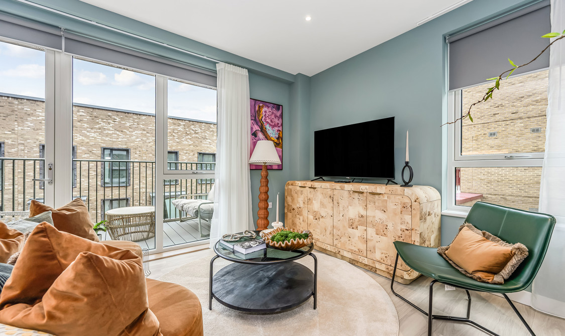 A contemporary living room featuring a large TV, sofa and arm chair, and plenty of natural light from the private balcony.