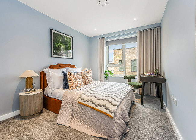 A bedroom with a cosy bed and a working desk in the corner.
