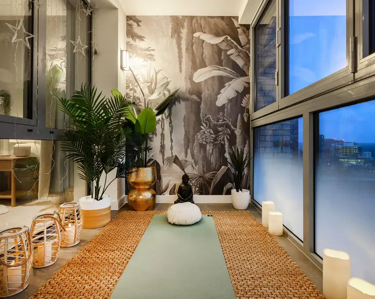 A winter garden with floor-to-ceiling windows, a yoga mat, indoor plants and a sweeping evening cityscape view.