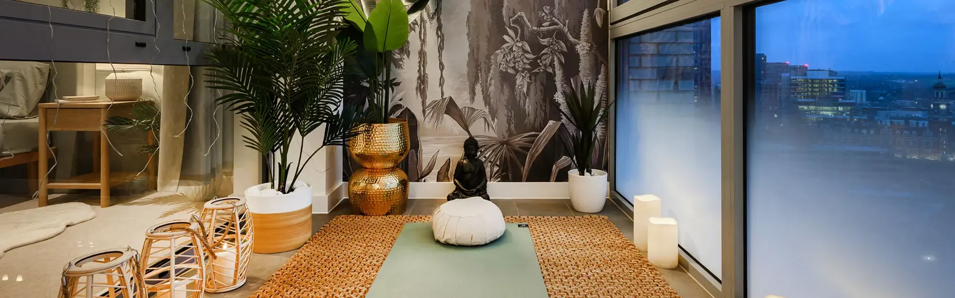 A winter garden with floor-to-ceiling windows, a yoga mat, indoor plants and a sweeping evening cityscape view.