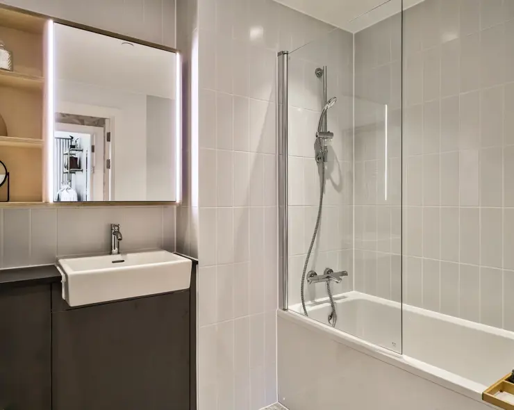 A bathroom with a over bath shower, fitted sinks and appliances and plenty of storage.