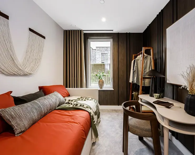 A contemporary single-bedroom with a working desk and open wardrobe.